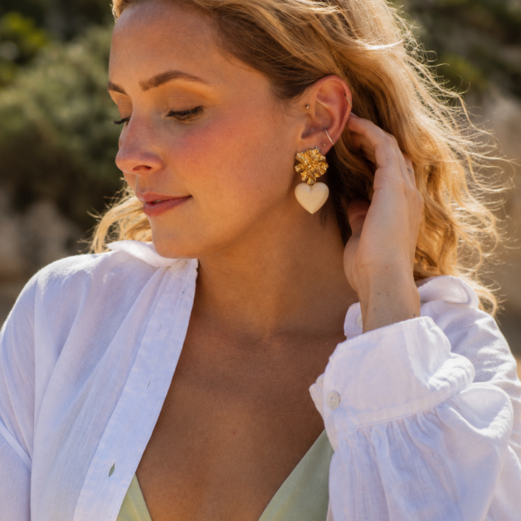 ChatGPT Image 17 mai 2026 20_41_00 | MAISON LIAMA Woman in a white blouse and pale green bikini top, wearing gold floral earrings with a heart pendant, eyes closed in a sunny outdoor setting.