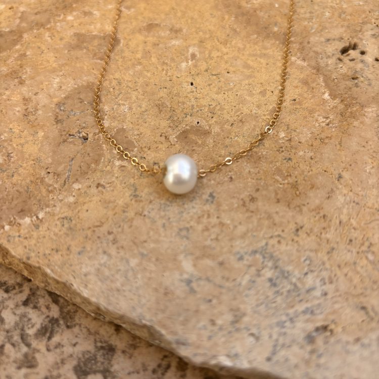 Gold chain necklace with a single white pearl pendant resting on a textured stone surface Bijoux créateur en ligne | MAISON LIAMA | Saint-Jean-de-Luz