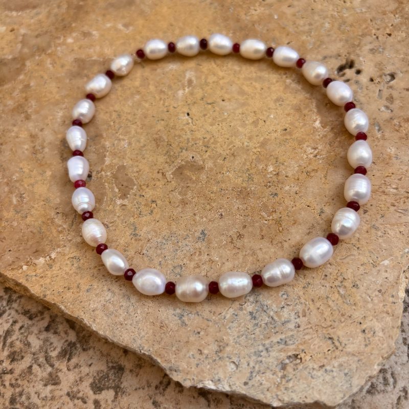 IMG_8351_800x800 | MAISON LIAMA Pearl bracelet with irregular white pearls and small red beads on a beige stone surface.