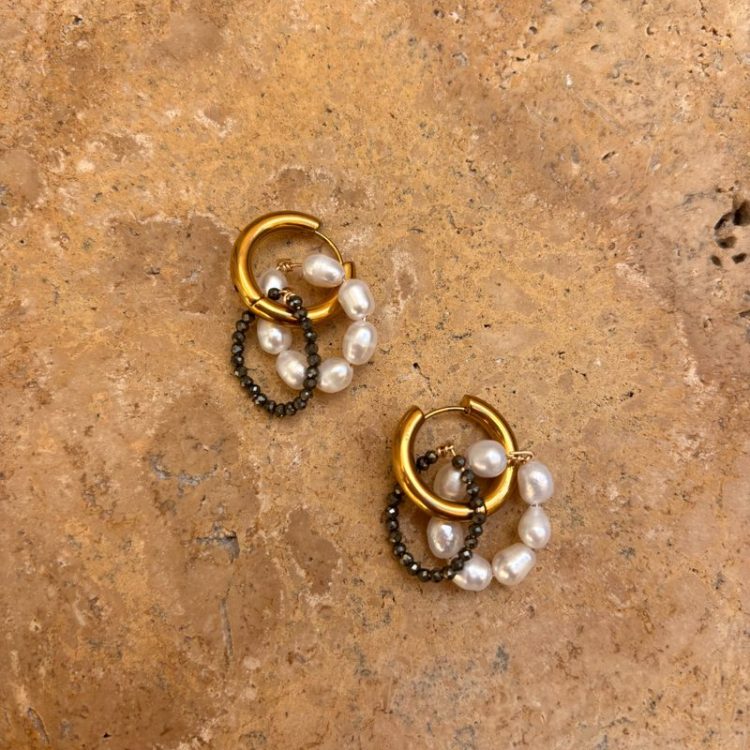 Gold hoop earrings with pearl strands and black bead accents on a textured beige surface.